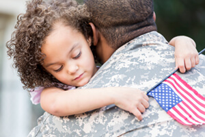 girl with a handheld american flag hugging a soldier