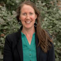 Headshot of Michelle Sikes wearing a green button-down shirt and navy jacket.