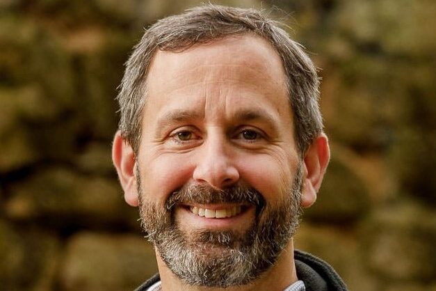 A headshot of David Kirk who is sporting a salt and pepper beard and mustache.