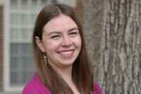 A headshot of Nicolette Bardele in front of a tree wearing a magenta blouse.