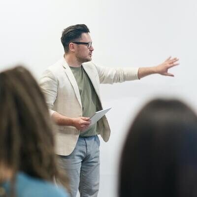 A person gesturing while lecturing in front of students.